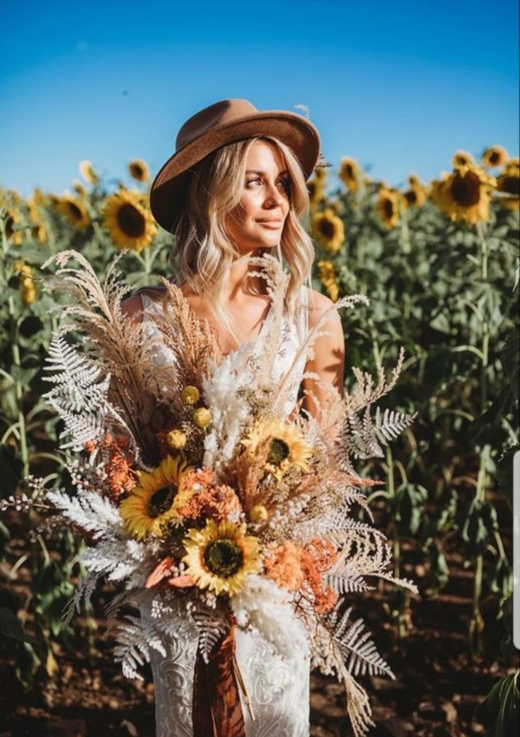 a woman standing in a field with sunflowers and holding a bouquet of flowers