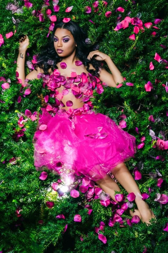 a woman laying in the grass surrounded by pink flowers with her hands on her hips