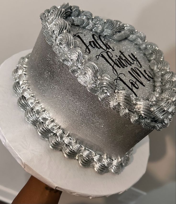 a birthday cake with silver frosting and writing on the top is sitting on a white pedestal