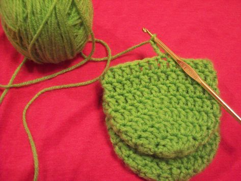 a green crochet pot holder with two balls of yarn next to it on a pink surface