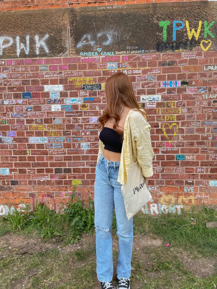 a woman standing in front of a brick wall with graffiti on it's walls