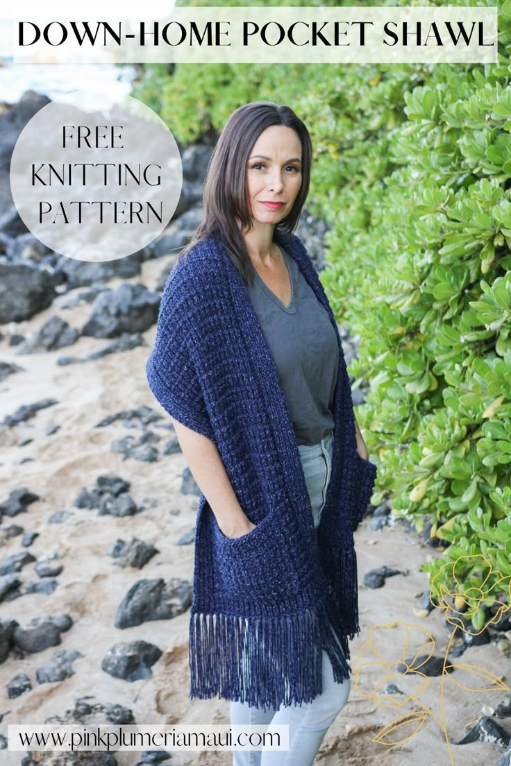 a woman standing on the beach wearing a blue knitted shawl with fringes