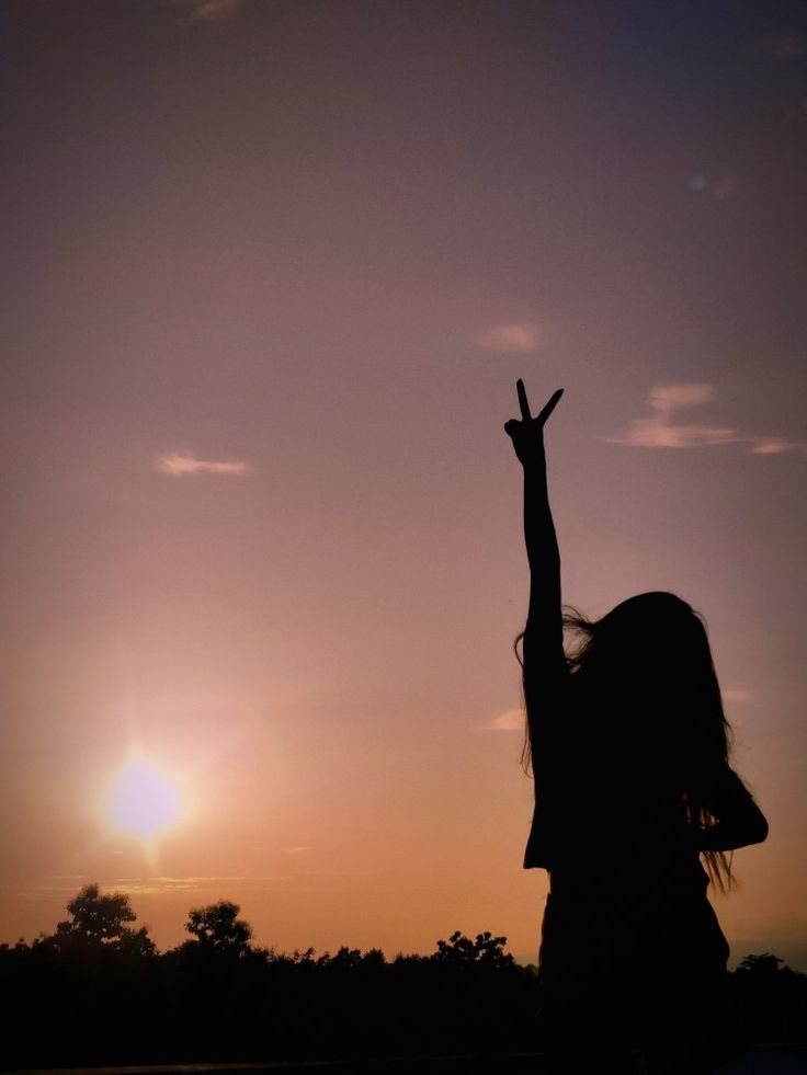 the silhouette of a woman with her arms up in the air, against a sunset