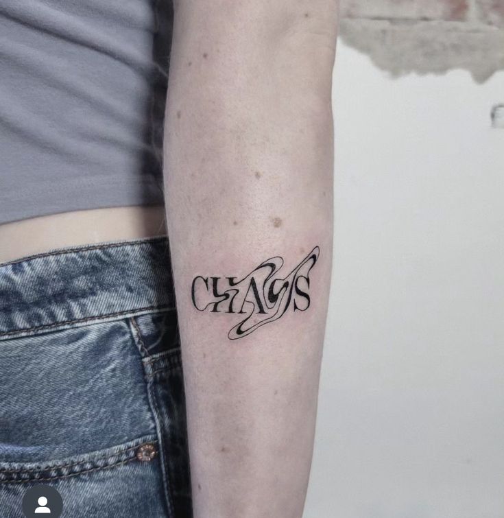 a person with a tattoo on their arm and the word chaos written in cursive writing