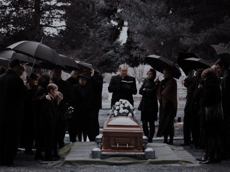 a group of people standing around a casket with umbrellas