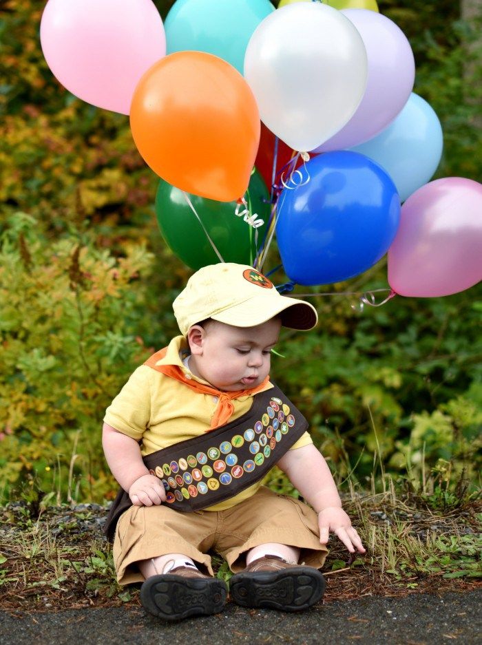 a young boy sitting on the ground with balloons attached to his hat and bib