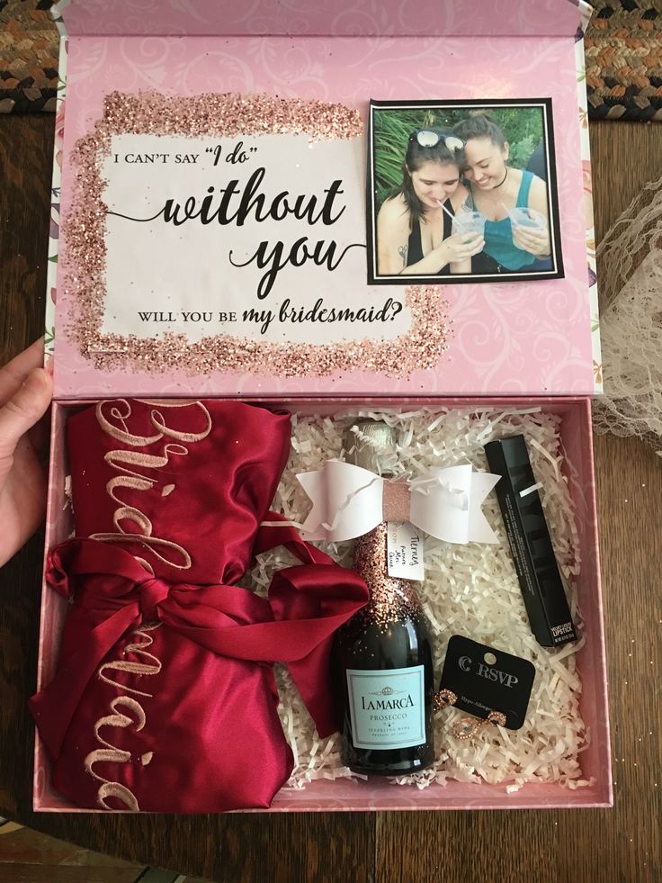 a pink box filled with personalized items on top of a wooden table next to a bottle of wine