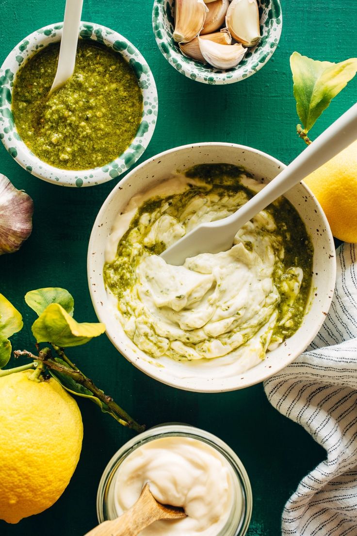 two bowls filled with pesto and lemons on top of a green tablecloth