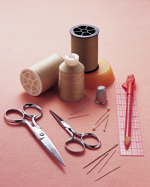 sewing supplies including scissors, spools and thread on a pink surface with a measuring tape