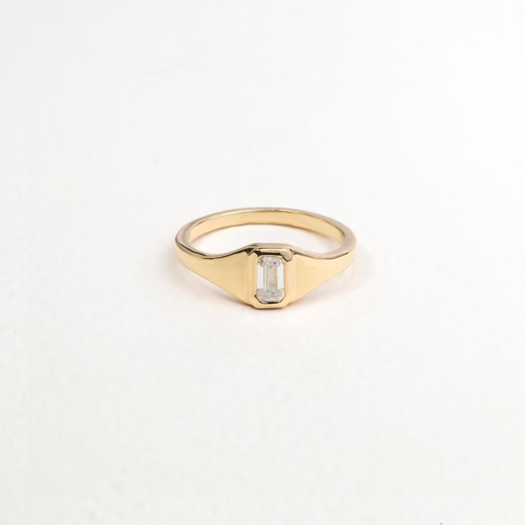 a yellow gold ring with an emerald stone set in the center, on a white background