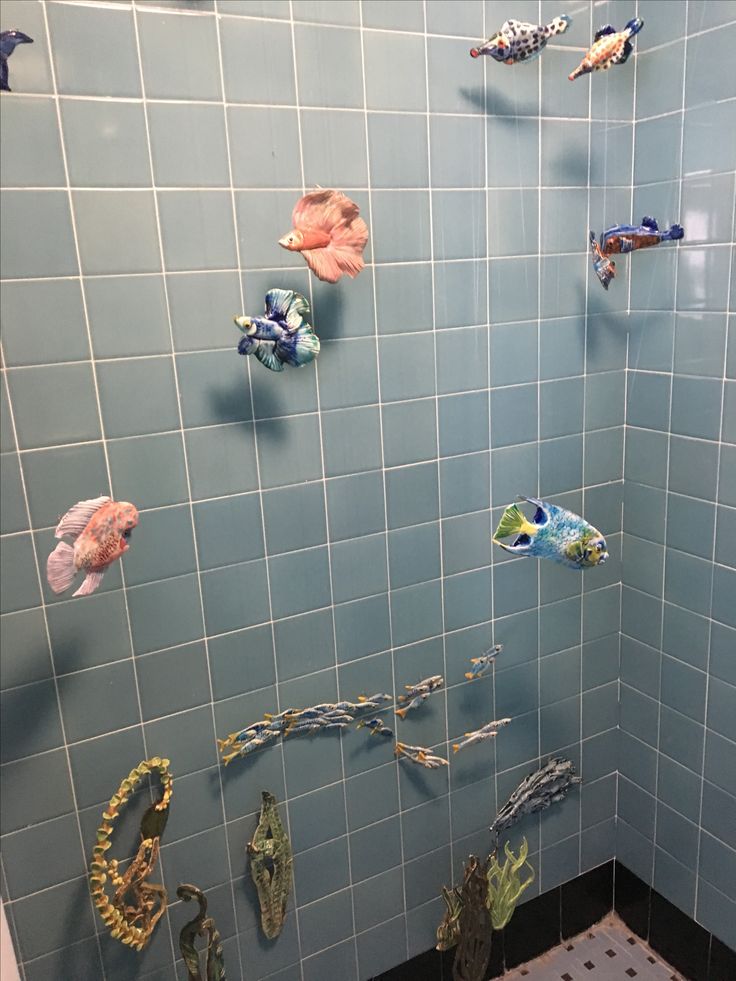 a bathroom with blue tiled walls and fish decorations on the shower wall, along with tile flooring