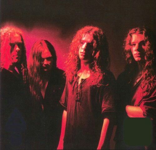 three men standing in front of a red light with long hair and wearing black clothing