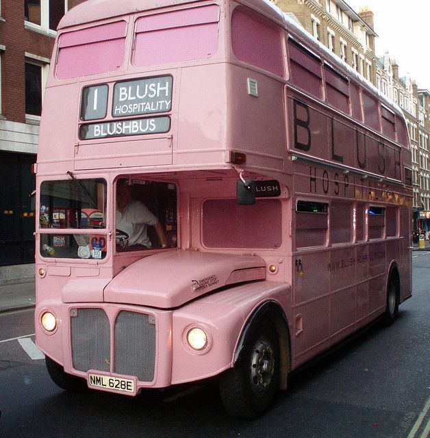 a pink double decker bus driving down the street