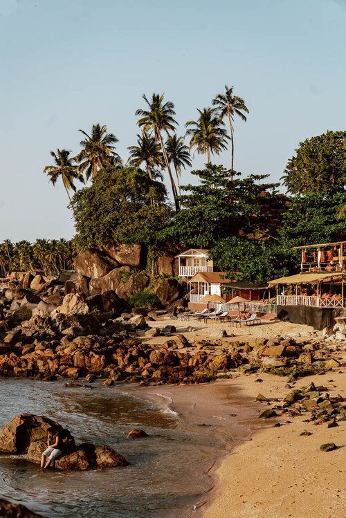 a sandy beach next to the ocean with houses on top of it and palm trees in the background