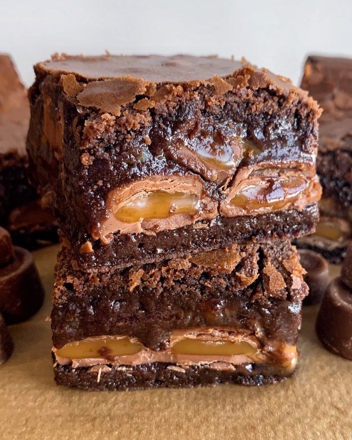 three chocolate brownies stacked on top of each other with caramels in the background