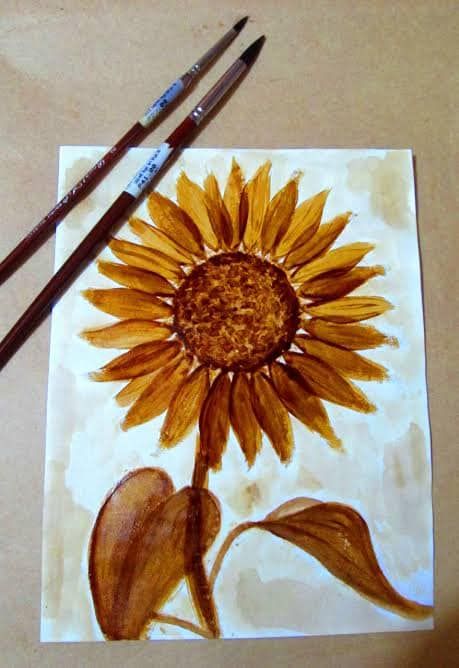 two brown and yellow sunflowers are on a piece of paper with watercolor pencils