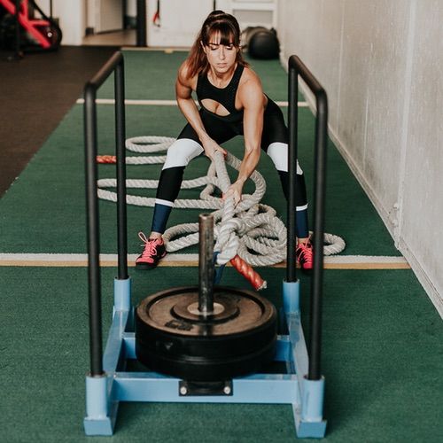 a woman in black shirt doing exercises on a blue exercise cart with ropes and rope