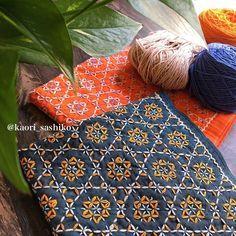 two balls of yarn are sitting on top of an orange and blue table cloth next to a potted plant