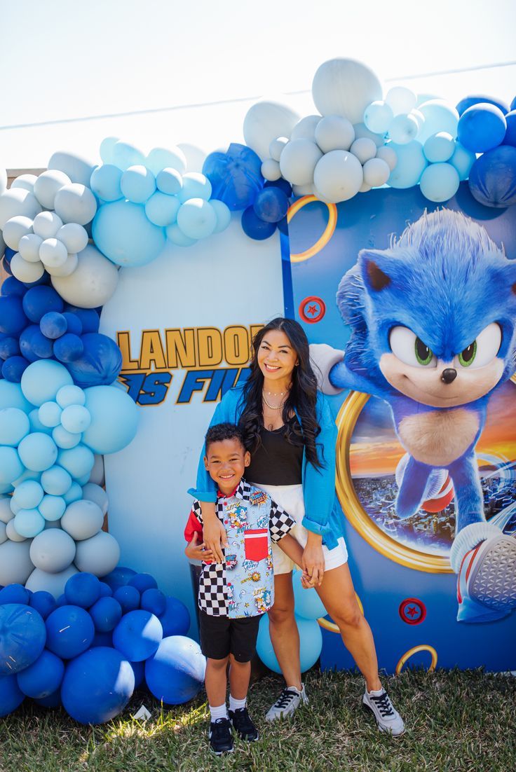 a woman standing next to a child in front of a balloon arch with sonic the hedgehog on it