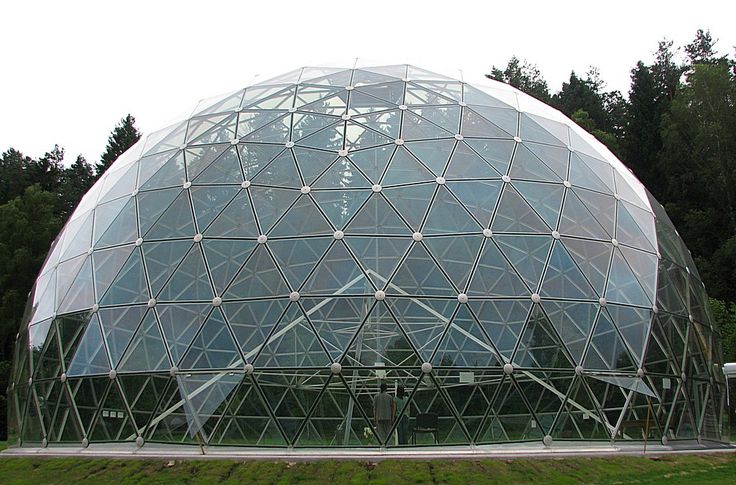 a large glass dome sitting on top of a lush green field next to a forest