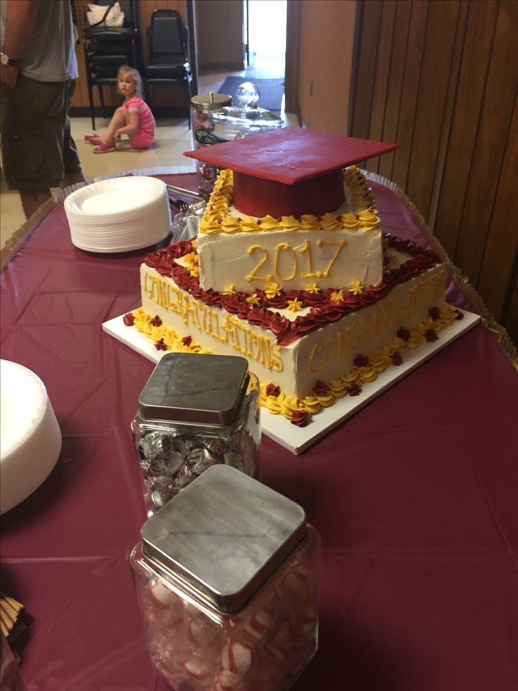 two tiered cake with graduation caps on top and candy in plastic containers sitting on the table