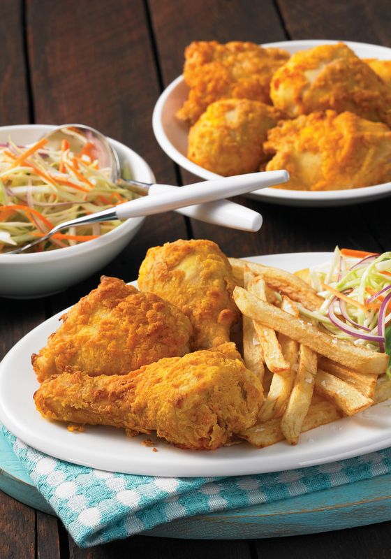 two plates with fried chicken and french fries next to a bowl of coleslaw