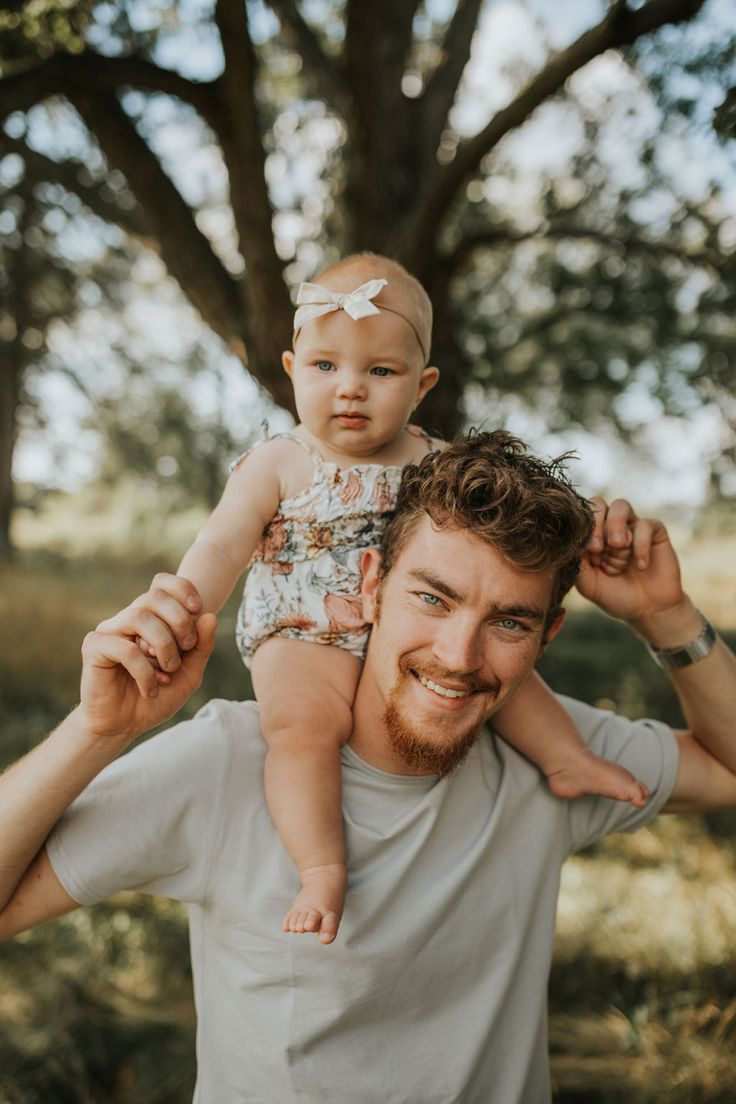 a man holding a baby up to his face in front of a tree while smiling at the camera