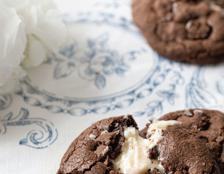 two chocolate cookies with ice cream are on a blue and white plate next to a flower