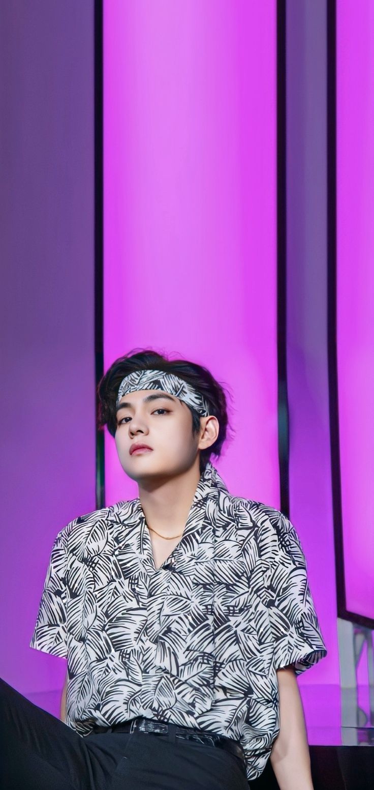 a young man sitting in front of a purple background wearing a head band and black pants