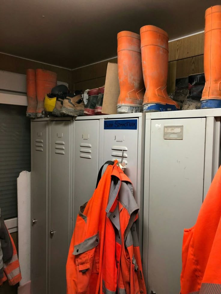 an orange life jacket is hanging on the lockers next to other safety jackets and boots