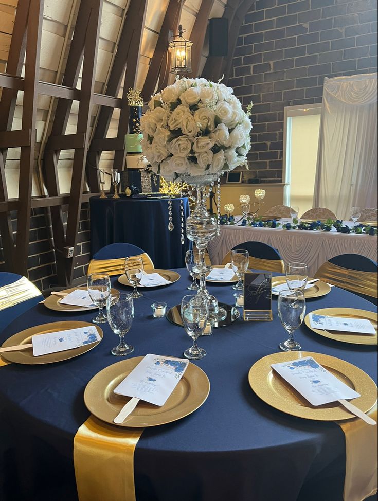 the table is set with blue linens and gold place settings, white flowers in vase