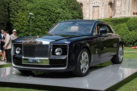 a black rolls royce parked on top of a cement platform in front of some bushes