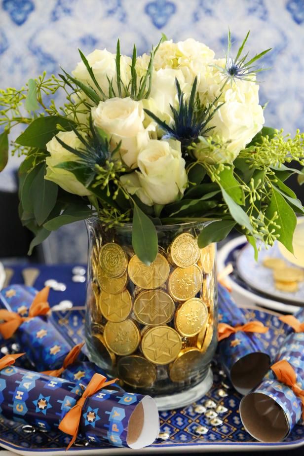 a vase filled with white roses and gold coins on top of a blue table cloth