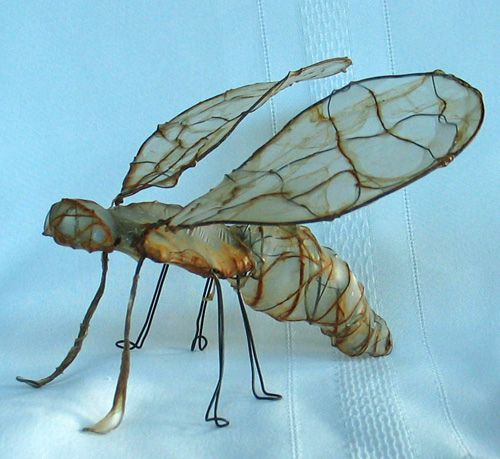 an insect made out of wire sitting on top of a white cloth covered tablecloth