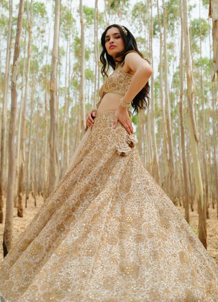 Elevate your style with a beige and gold floral embroidered lehenga, perfectly paired with an encrusted blouse and dupatta. This ensemble seamlessly blends intricate detailing with modern sophistication, creating a refined and stylish look for special occasions. Bronze Lehenga, Leaf Sleeve, Embroidered Motifs, Beige Silk, Embroidered Lehenga, Embroidered Border, French Knots, Gold Floral, Silk Thread