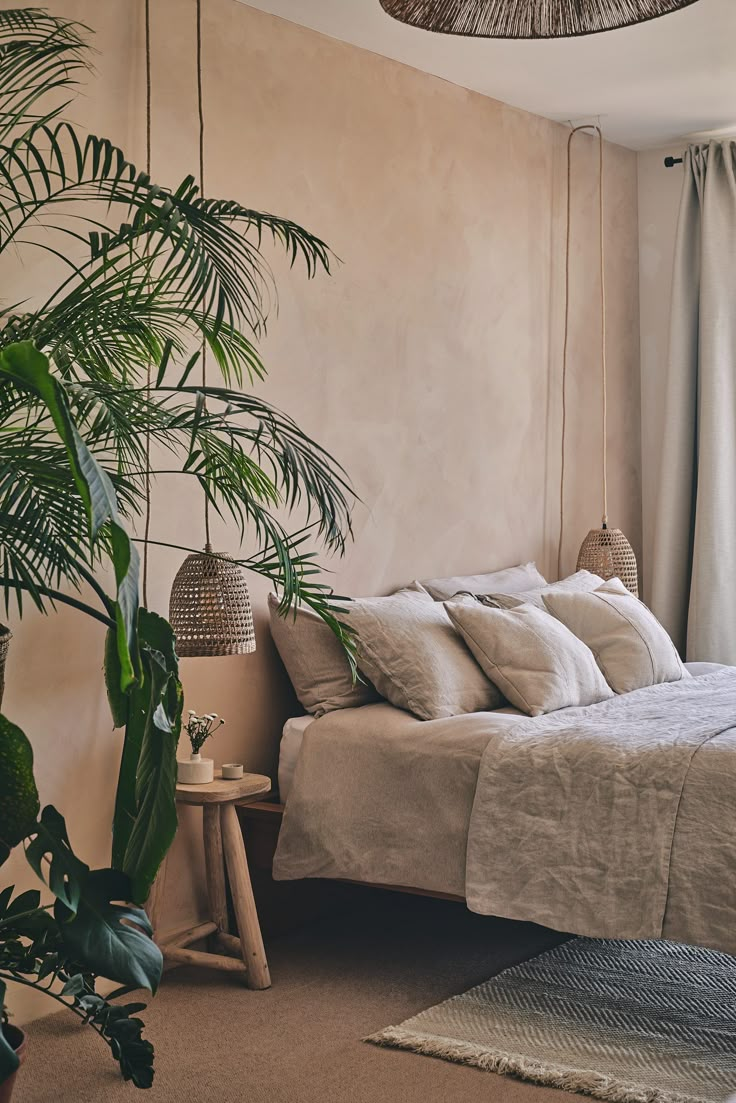 a bed sitting next to a tall plant in a bedroom under a light colored wall