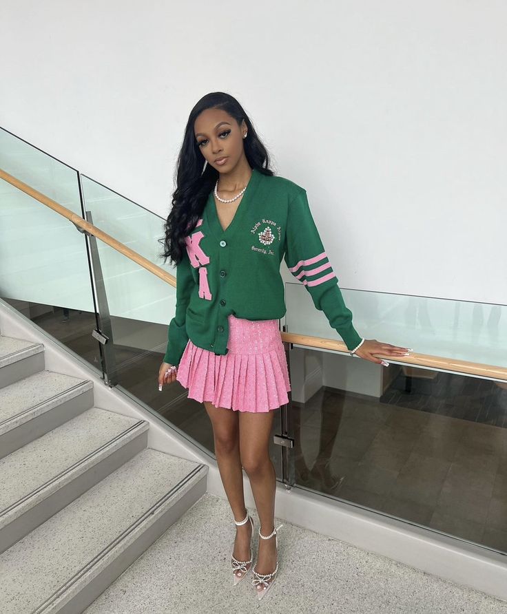 a woman standing in front of some stairs wearing a green cardigan and pink skirt