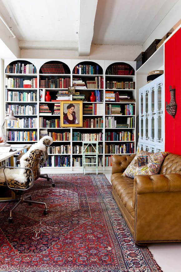 a living room filled with lots of furniture and bookshelves next to a red door