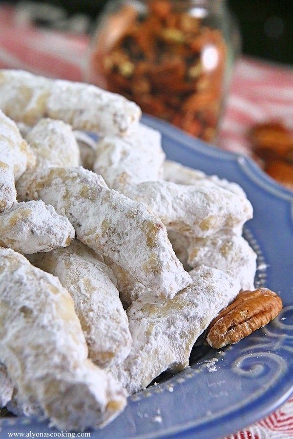 a blue plate topped with powdered sugar cookies and pecans next to a jar of nuts