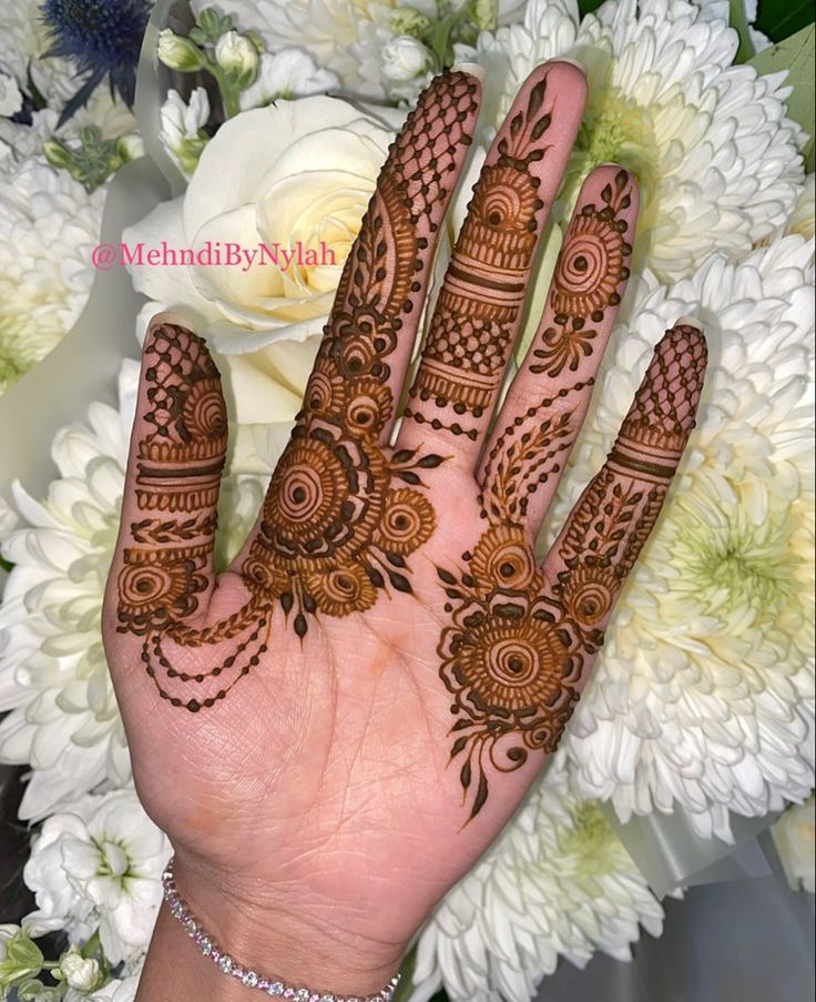 a hand with henna on it and flowers in the background