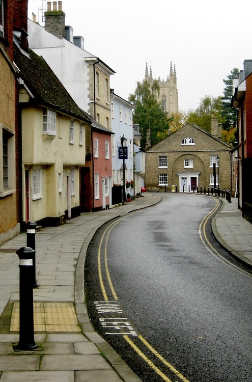 an empty street with buildings on both sides and a clock tower in the background,