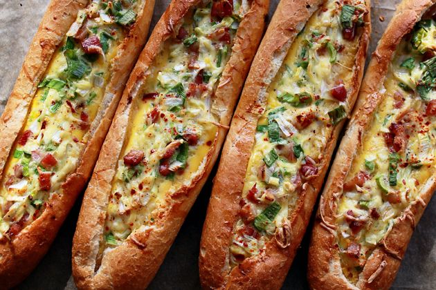 four breads with cheese and toppings on them sitting on a piece of parchment paper