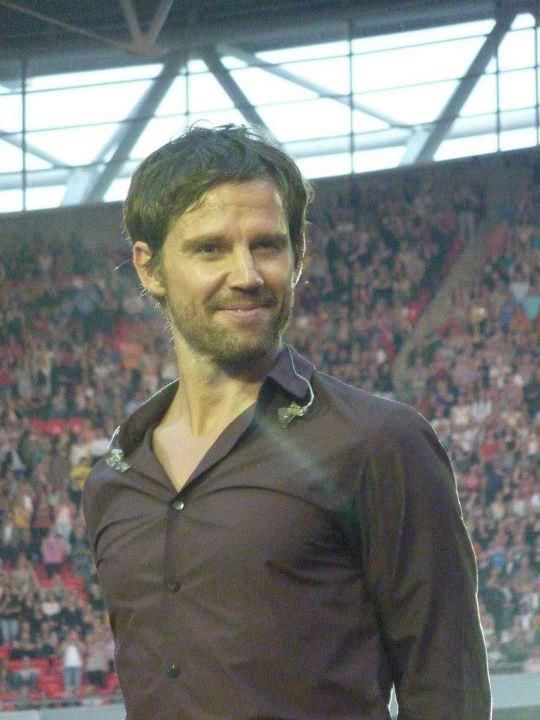 a man standing in front of a large crowd at a soccer game wearing a brown shirt