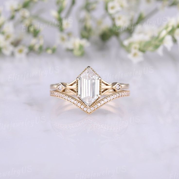 a white diamond ring sitting on top of a table next to some flowers and greenery