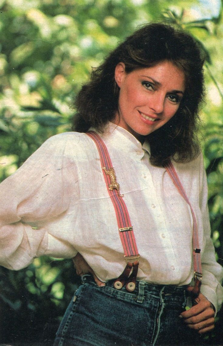 a woman wearing suspenders and a white shirt is posing for the camera with her hands on her hips