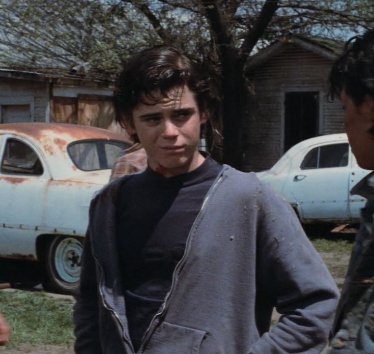 two young men standing next to each other in front of an old car and house