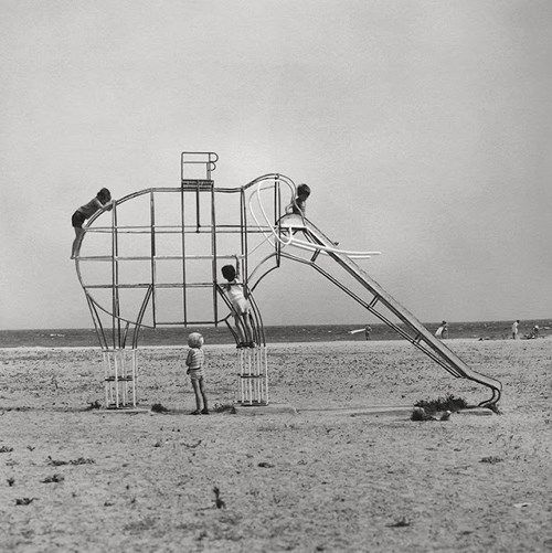 two children are playing in the sand next to a large metal structure that looks like an elephant