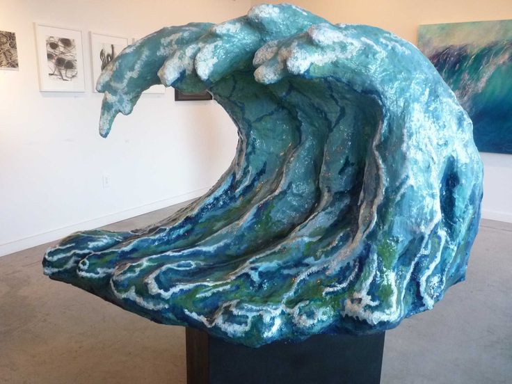 a large blue wave sculpture sitting on top of a black pedestal in a room with pictures on the wall