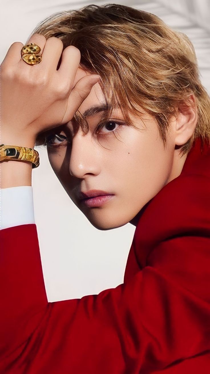 a young man wearing a red shirt and gold bracelet with his hand on his head