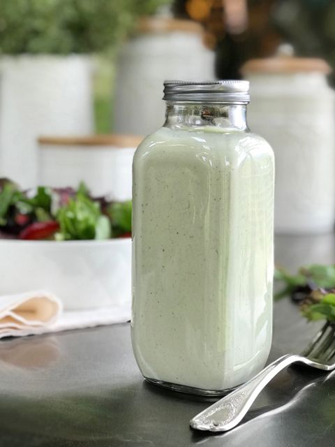 a glass jar filled with green liquid sitting on top of a table next to a salad